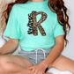 A person wearing a mint green t-shirt with a leopard print design and gray shorts is sitting on the floor.
