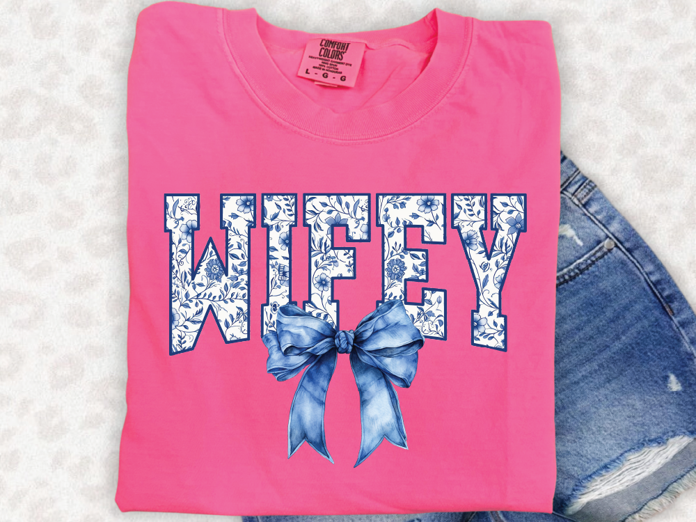 A pink t-shirt with the word "WIFEY" printed on it, along with a blue bow.