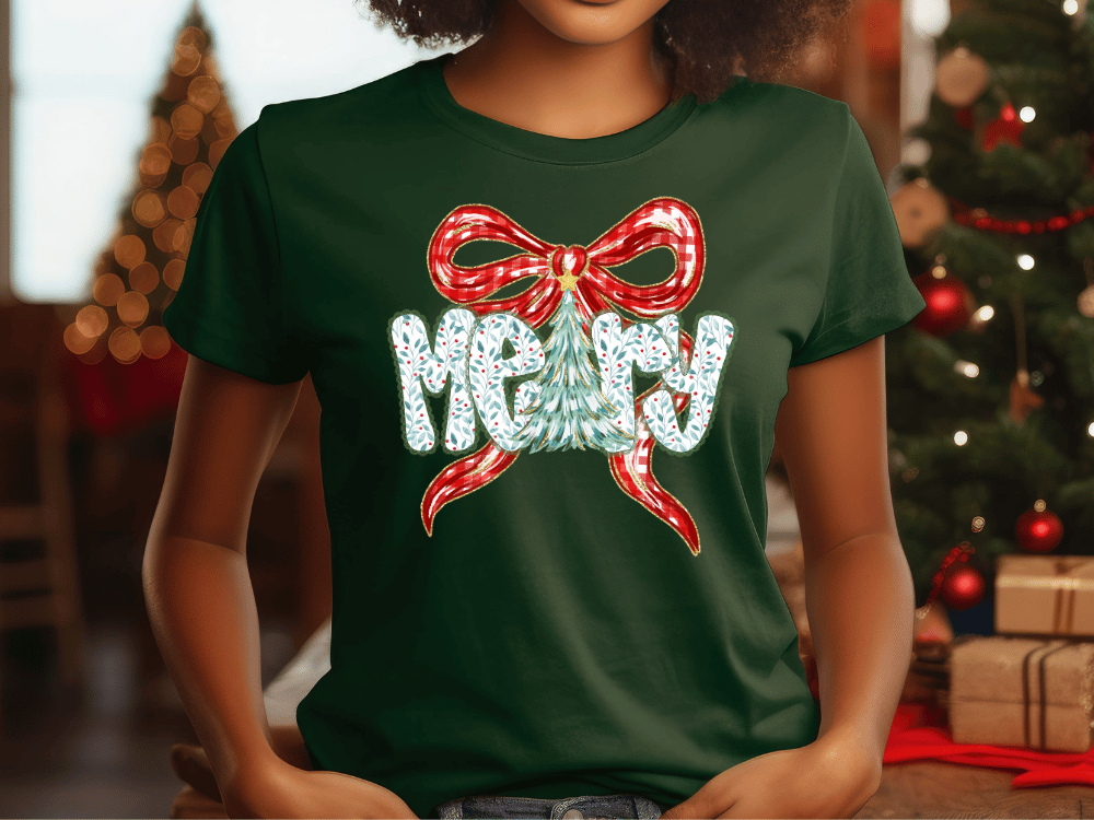 A woman wearing a green t-shirt with a red bow and the word "Merry" printed on it, standing in front of a Christmas tree.