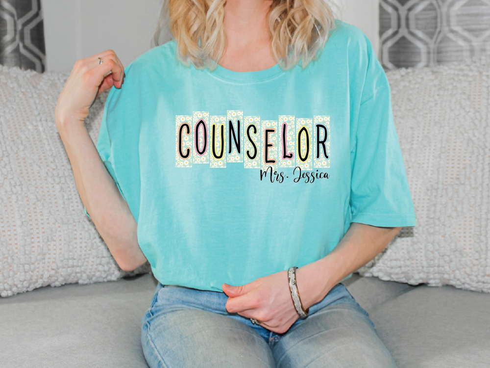 A woman wearing a light blue t-shirt with the text "COUSELLOR" and "Mrs. Jessica" printed on it, sitting on a couch.