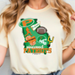 A person wearing a white t-shirt with a graphic design featuring various sports-related elements, including a football, cheerleaders, and the text "Patriots" and "Pinewood Patriots".