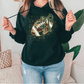 A woman wearing a black hoodie with a football graphic and a green bow, standing in a room with a couch and a plant.