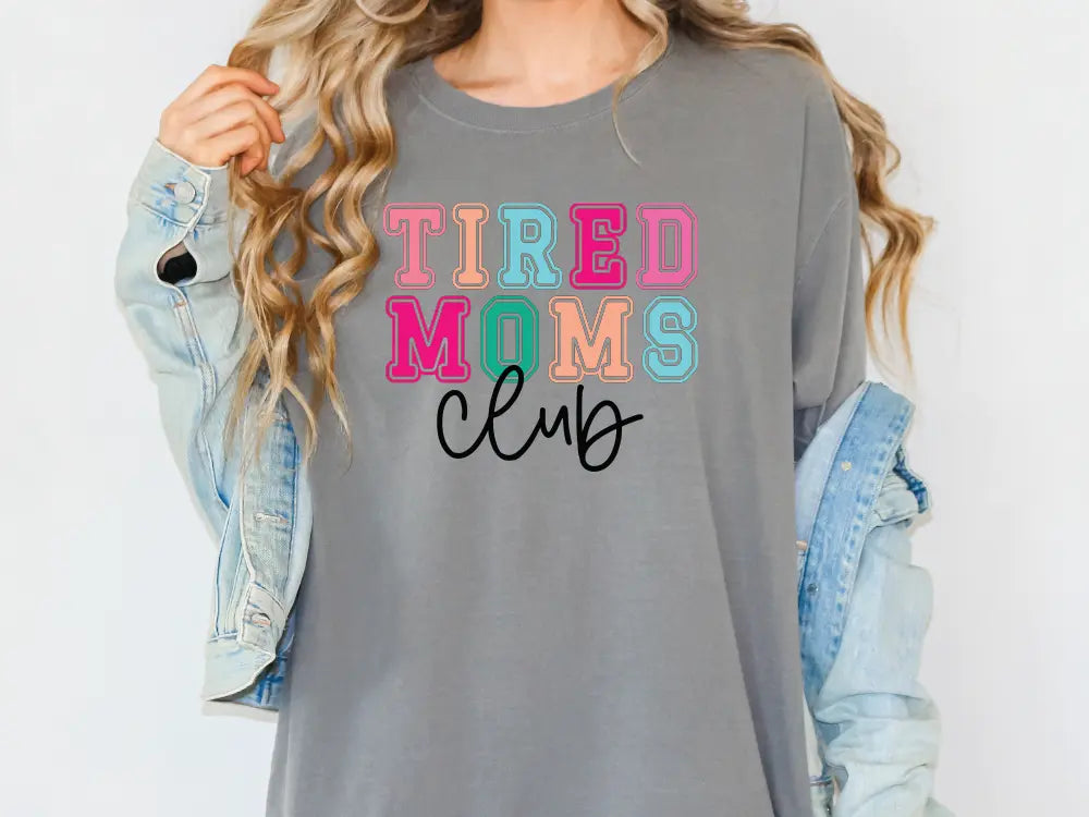 a woman wearing a grey tired moms club shirt