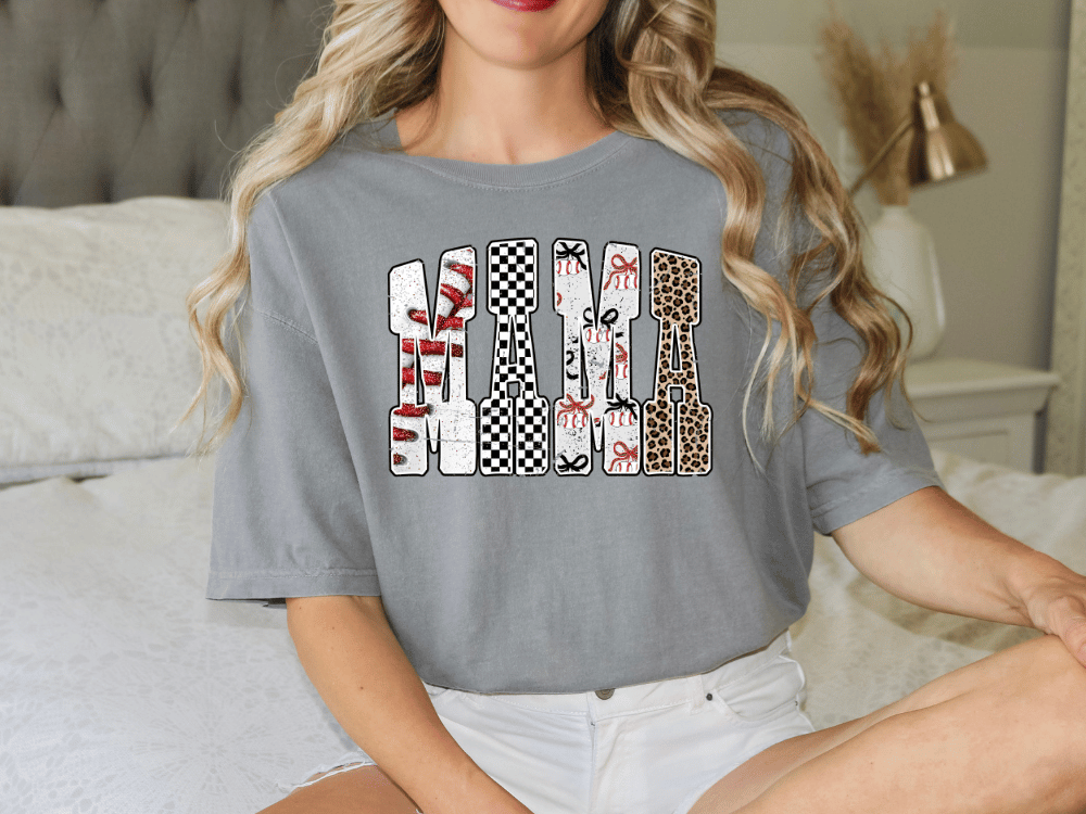 A woman wearing a grey t-shirt with a graphic design on it, sitting on a bed.