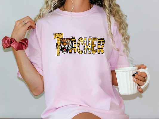 A woman wearing a pink t-shirt with the word "Teacher" printed on it, holding a white mug in her hand.
