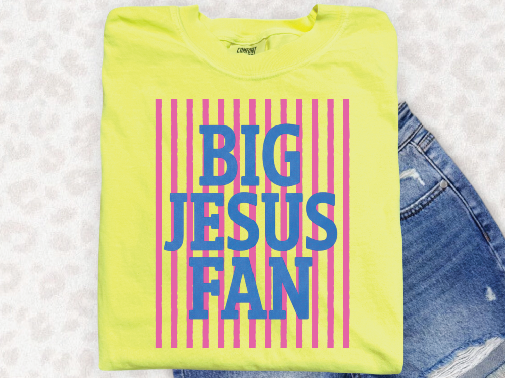 A yellow t-shirt with the text "BIG JESUS FAN" printed on it, along with vertical stripes in pink and blue.