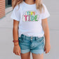 a little girl standing on a sidewalk wearing a t - shirt that says tiny tide