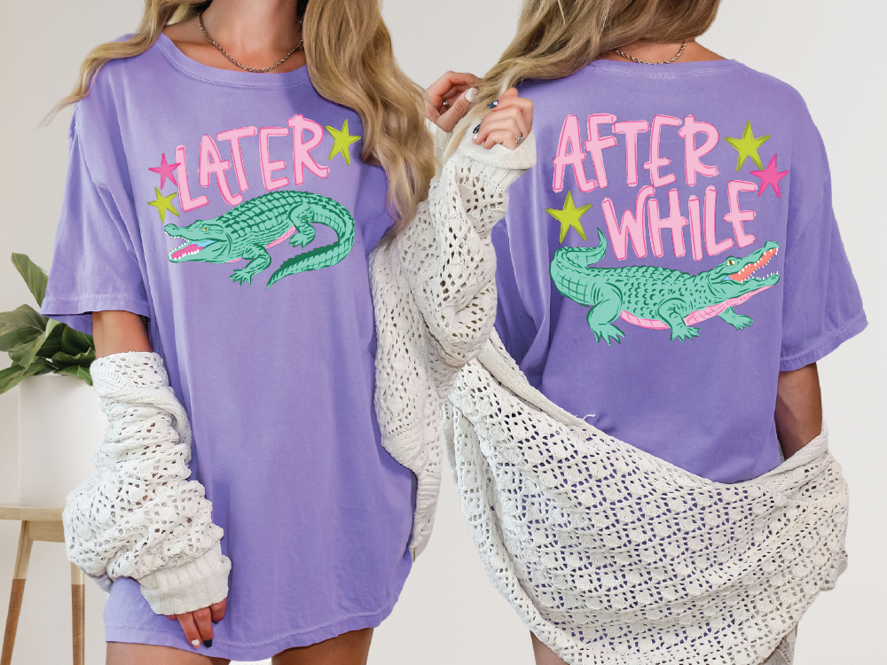 two women wearing purple t-shirts with a graphic of a green alligator and the text "LATER" and "AFTER WHILE" printed on them.