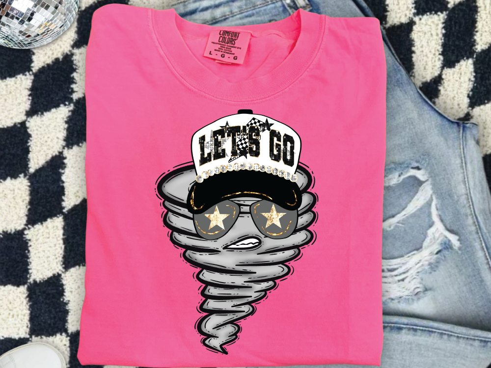 A pink t-shirt with a graphic design of a stormy-looking character wearing sunglasses and a baseball cap, along with the text "LET'S GO" printed on it.