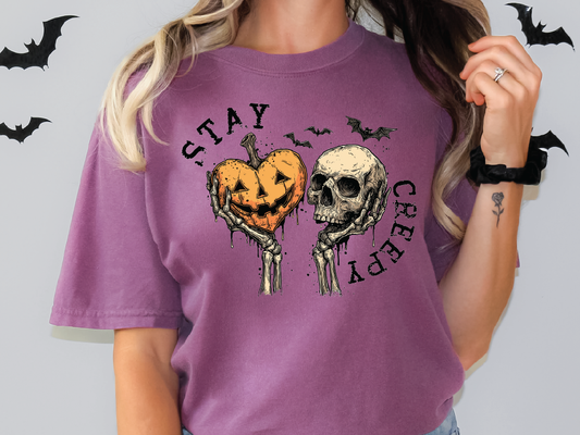 A woman wearing a purple t-shirt with a graphic design featuring a pumpkin and a skull, along with the text "STAY CREEPY" and bats.
