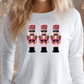 A woman wearing a white long-sleeved shirt with a design of three nutcracker men in pink and gold outfits.