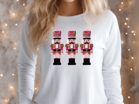 A woman wearing a white long-sleeved shirt with a design of three nutcracker men in pink and gold outfits.