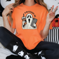 a woman sitting on a bed wearing an orange shirt with a ghost on it