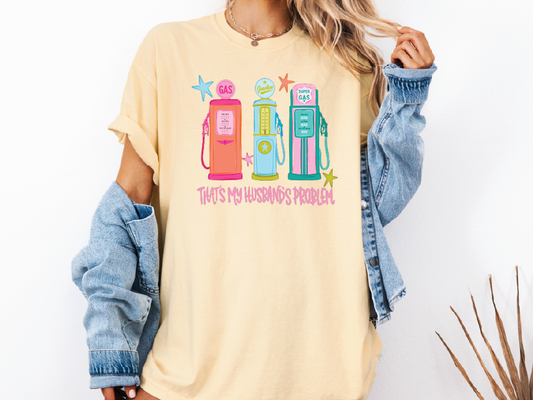 A woman wearing a yellow t-shirt with a graphic design of three colorful gas pumps and the text "That's my husband's problem" printed on it.