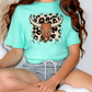 A woman wearing a turquoise t-shirt with a graphic of a bull's head and leopard print accents.