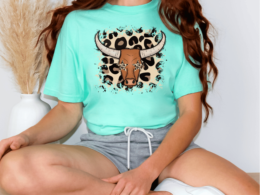 A woman wearing a turquoise t-shirt with a graphic of a bull's head and leopard print accents.