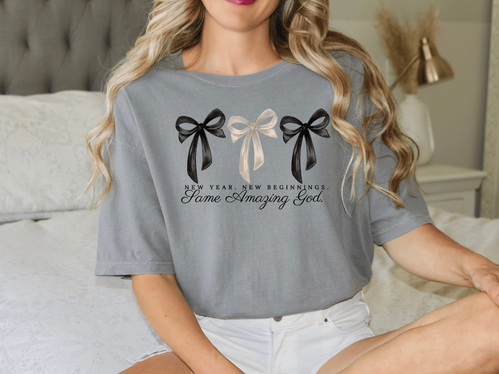 A woman wearing a gray t-shirt with a graphic design of three bows and the text "New Year, new beginnings. Some amazing God."