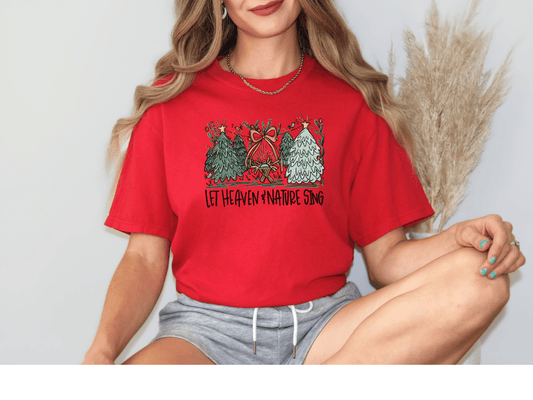 A woman wearing a red t-shirt with a Christmas-themed graphic and text, sitting with her legs crossed.