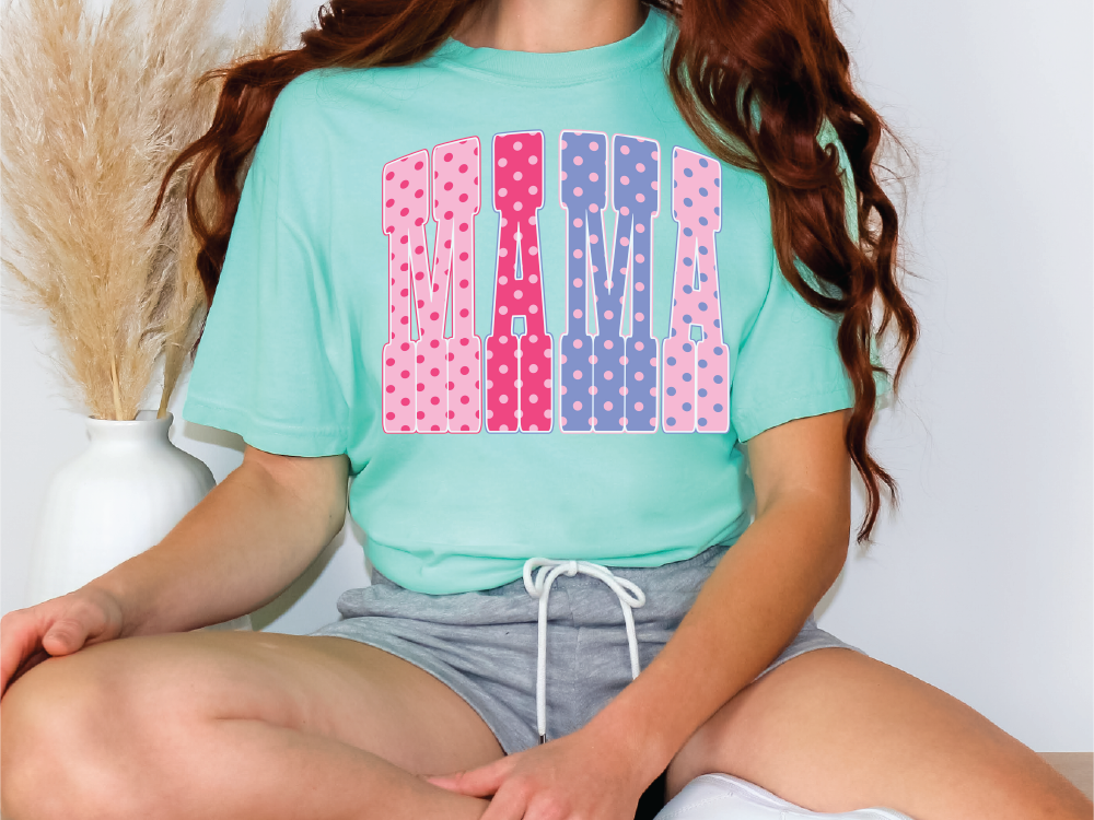 A woman wearing a green t-shirt with pink and blue polka dots and gray shorts is sitting on a chair.