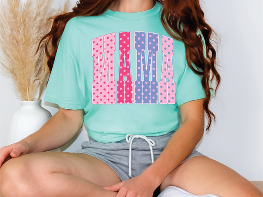 A woman wearing a green t-shirt with pink and blue polka dots and gray shorts is sitting on a chair.