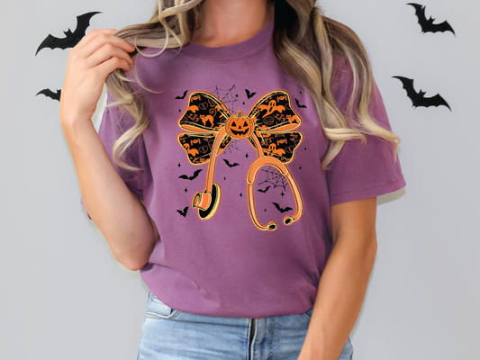 A woman wearing a purple t-shirt with a Halloween-themed graphic design, including a large bow, bats, and a pumpkin.