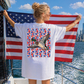 A woman stands on a boat holding an American flag, with a city skyline visible in the background.