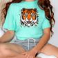 A person wearing a turquoise t-shirt with a tiger graphic and gray shorts is sitting on the floor.