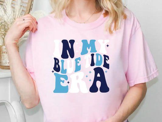 a woman wearing a pink shirt that says, i'm my blue tide era