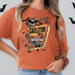 A woman wearing an orange t-shirt with a graphic design of a skeleton motel and bats.