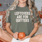 A woman sitting on a bed, wearing a green t-shirt with the text "Leftovers are for quitters" printed on it. She is holding a pumpkin-shaped mug in her hands.