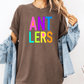 A person wearing a brown t-shirt with the text "ANT LERS" in colorful letters, paired with a denim jacket.