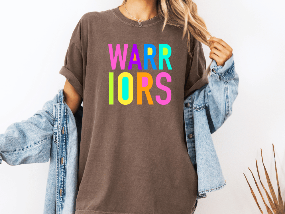 A person wearing a brown t-shirt with the text "WARRIORS" in colorful letters, paired with a denim jacket.