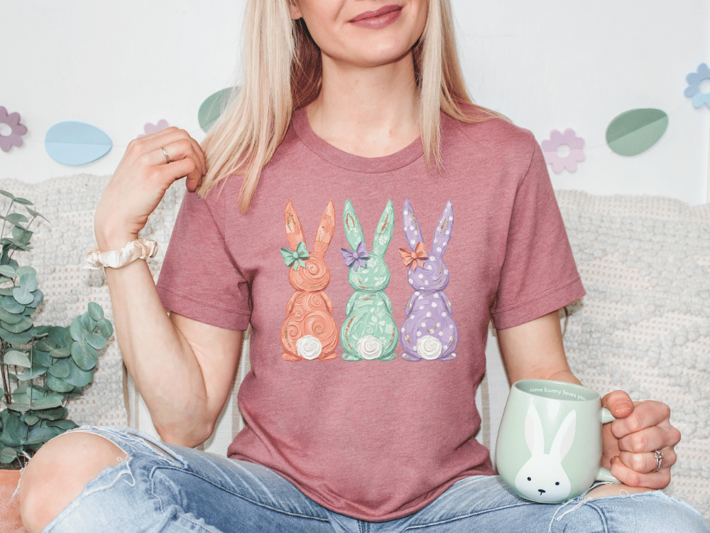 A woman wearing a pink t-shirt with a bunny design is sitting on a couch, holding a mug and smiling.