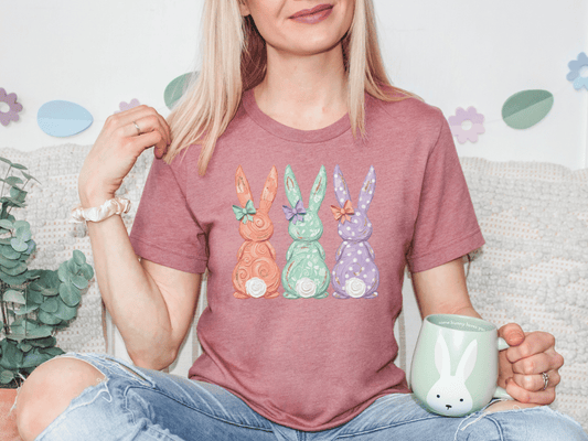 A woman wearing a pink t-shirt with a bunny design is sitting on a couch, holding a mug and smiling.