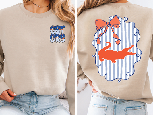 The image is a collage of two photos. The left photo shows a person wearing a beige sweater with a blue and white striped design on the front, featuring a graphic of a cat. The right photo shows the back of the same sweater, with a graphic of a cat and a bow on the back.