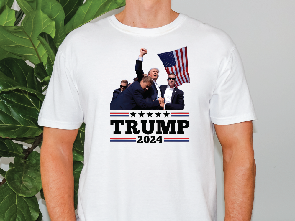 a man wearing a trump t - shirt in front of a plant