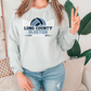 A woman wearing a gray sweatshirt with the text "LONG COUNTY BLUE TIDE VOLLEYBALL" printed on it, standing in front of a plant.