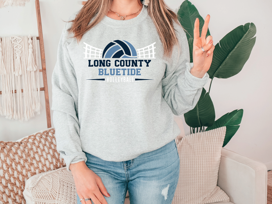 A woman wearing a gray sweatshirt with the text "LONG COUNTY BLUE TIDE VOLLEYBALL" printed on it, standing in front of a plant.