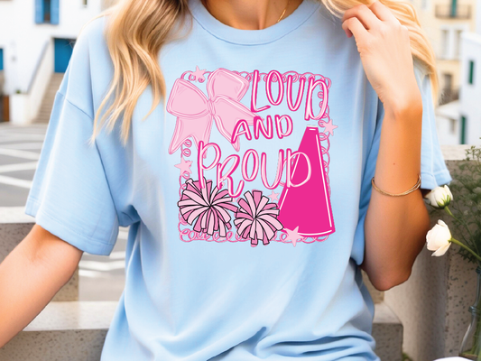 A woman wearing a light blue t-shirt with a graphic design featuring a pink cheerleader, flowers, and the text "LOUD AND PROUD".