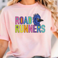 A woman wearing a pink t-shirt with the text "ROAD RUNNERS" printed on it.