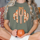 A woman is sitting on a couch, wearing a green t-shirt with a graphic design of a pumpkin and autumn leaves. She is holding a mug in her hands.