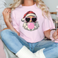 a woman sitting on a bed wearing a pink shirt with a santa clause on it