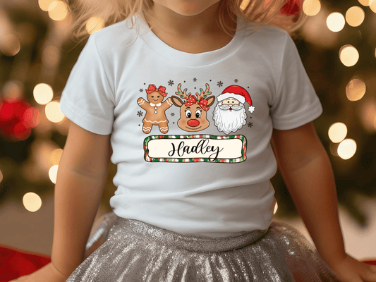A child wearing a white t-shirt with a Christmas-themed design featuring a reindeer, Santa Claus, and gingerbread men.