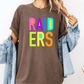 A person wearing a brown t-shirt with the word "RAIDERS" in colorful letters, paired with a denim jacket, stands against a white background.