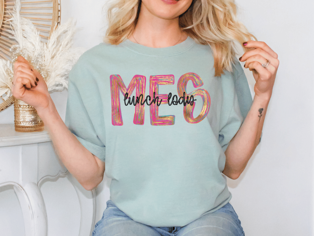 A woman wearing a light blue t-shirt with the text "lunch ladies" printed on it, sitting in front of a white wall.