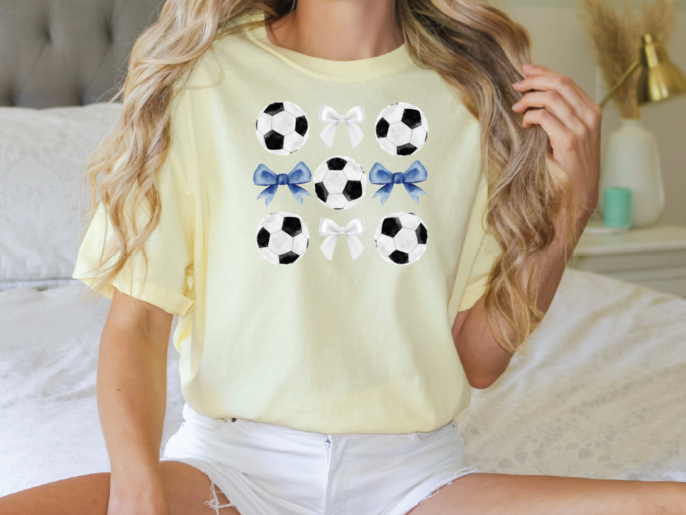 a woman sitting on a bed wearing a yellow shirt with soccer balls on it