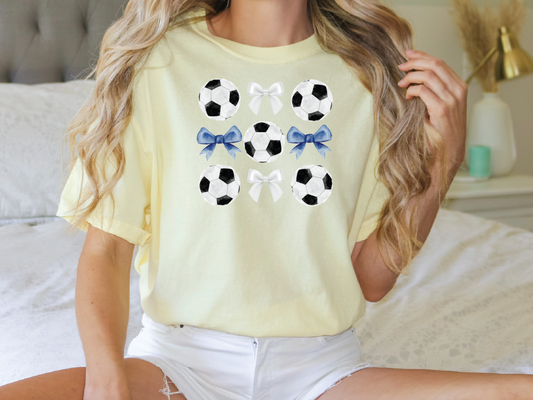 a woman sitting on a bed wearing a yellow shirt with soccer balls on it