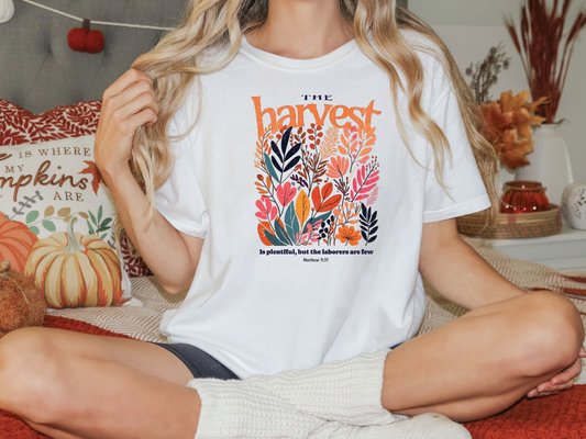 a woman sitting on a bed holding onto a harvest t - shirt