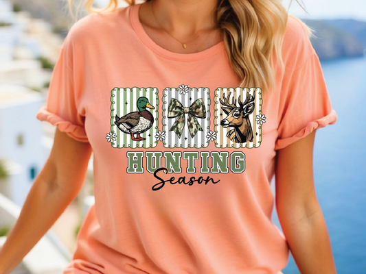 A woman wearing a peach-colored t-shirt with a graphic design featuring a duck, deer, and bow tie, along with the text "Hunting Season".