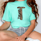 A person wearing a turquoise t-shirt with a leopard print design and gray shorts is sitting on the floor.